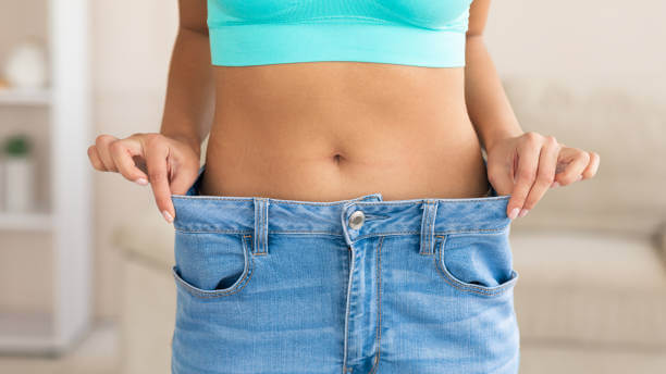 A woman holding out the waistband of loose-fitting pants, showcasing her successful weight loss results after peptide therapy.