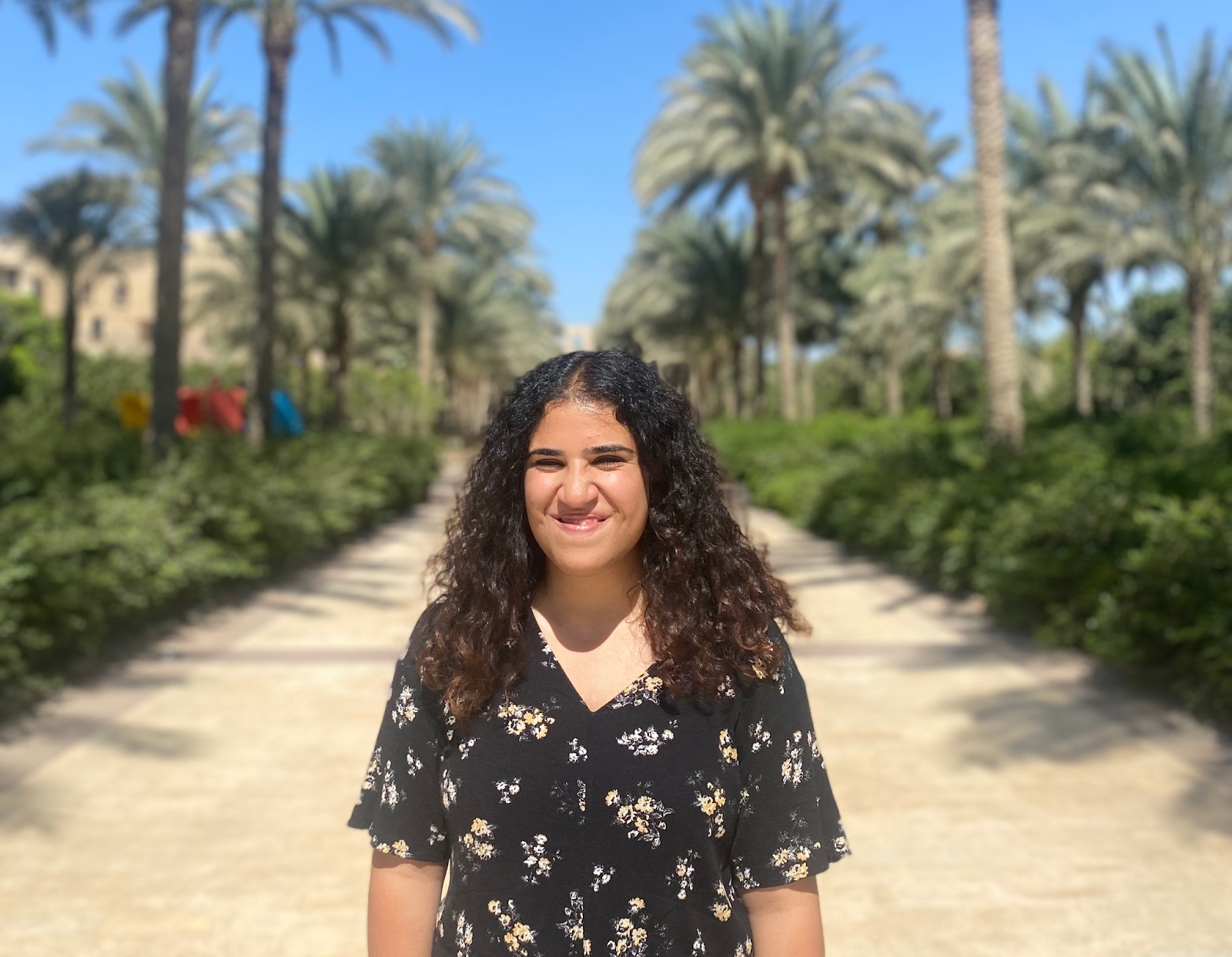 Girl smiles while standing in the central walkway of the AUC garden, palm trees in the background