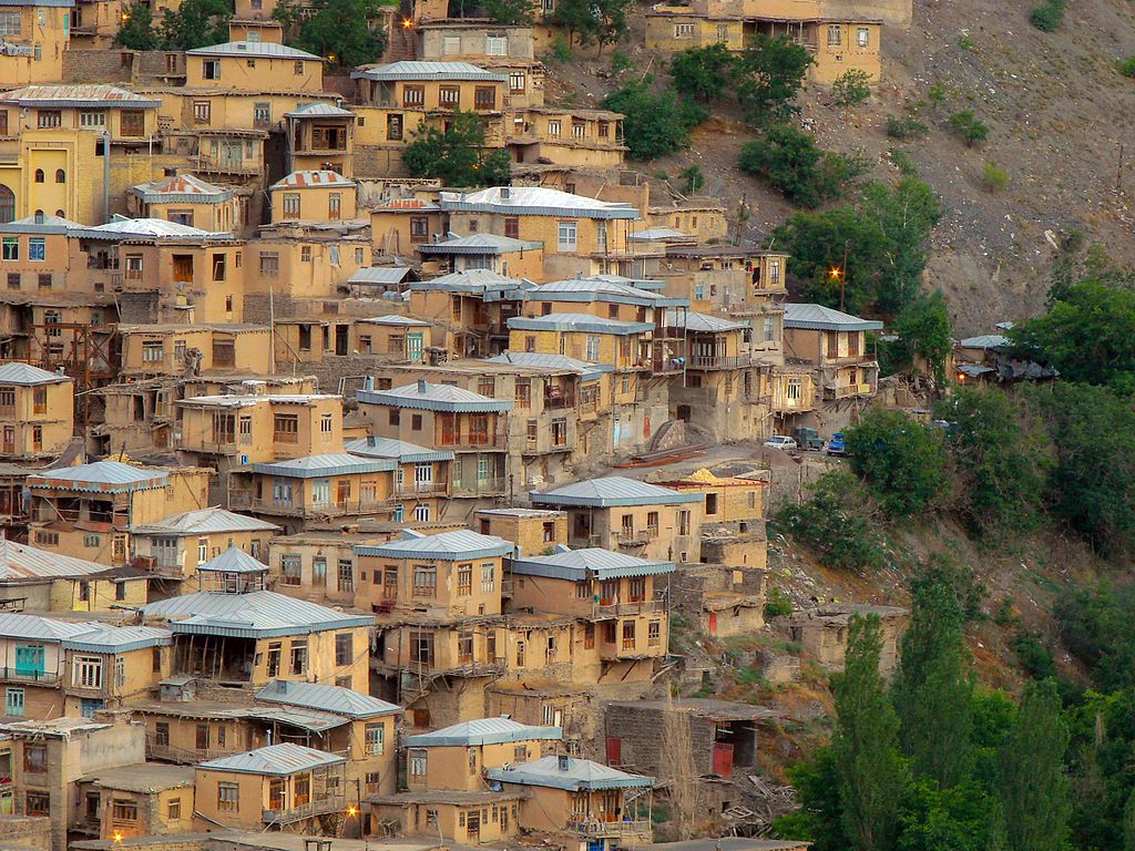 Scenic view of Kang Village in Khorasan, Iran, showcasing traditional stone and mud-brick houses built into the mountainside, with narrow streets and lush greenery surrounding the village.