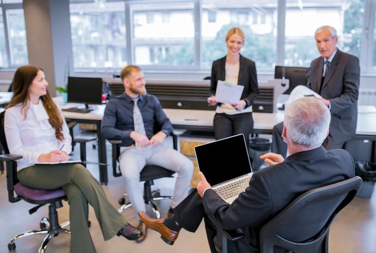 Senior businessman sitting on chair with laptop sitting in front of his team in the office