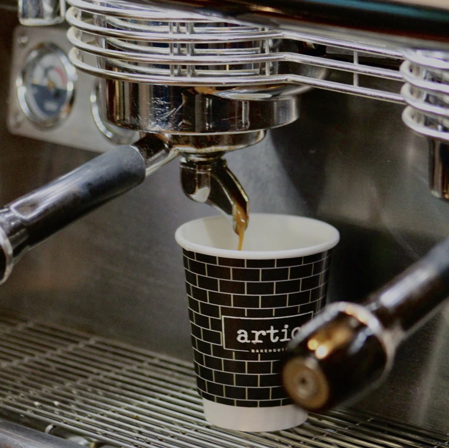 A coffee machine dispensing a fresh shot of espresso into a black coffee cup with a brick wall pattern and logo