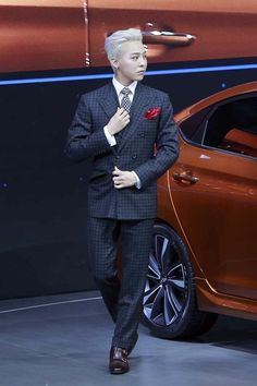 This contains an image of G-dragon in a suit and tie standing next to a car