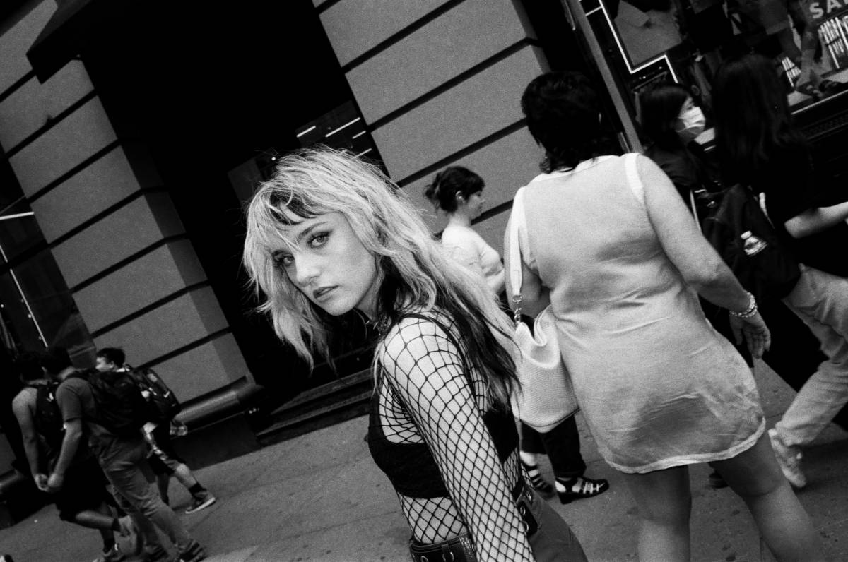 A black and white photograph of a young woman with black and blond hair, wearing a lace shirt