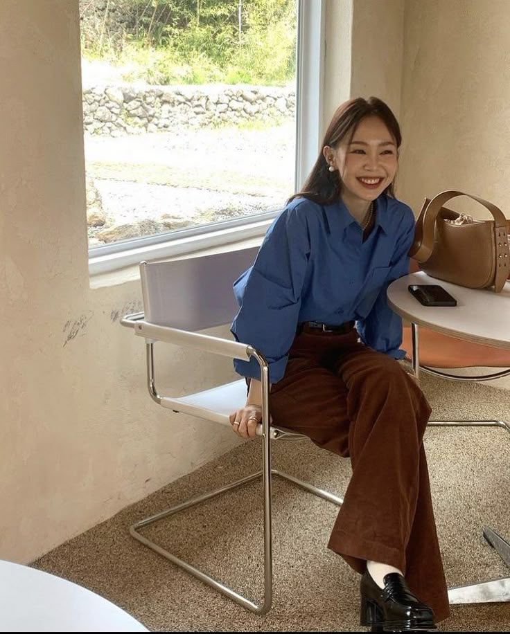 seorang wanita memakai kemeja biru dan celana cokelat tertawa sambil duduk