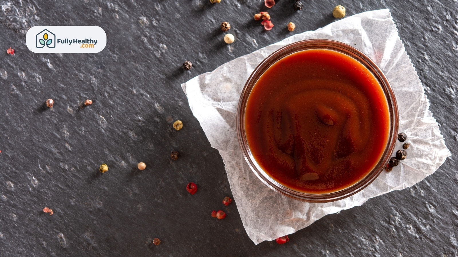 Bowl of barbecue sauce with scattered peppercorns on slate
