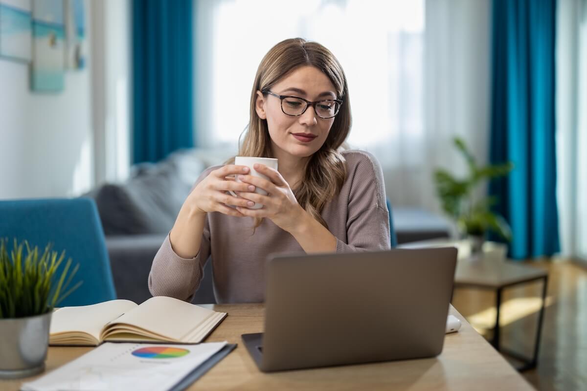 Employee holding a cup of coffee while looking at her laptop