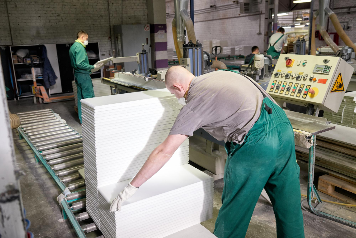 A worker bends over a conveyor belt in an awkward posture, a risk identified by an ergonomics assessment checklist for manufacturing.