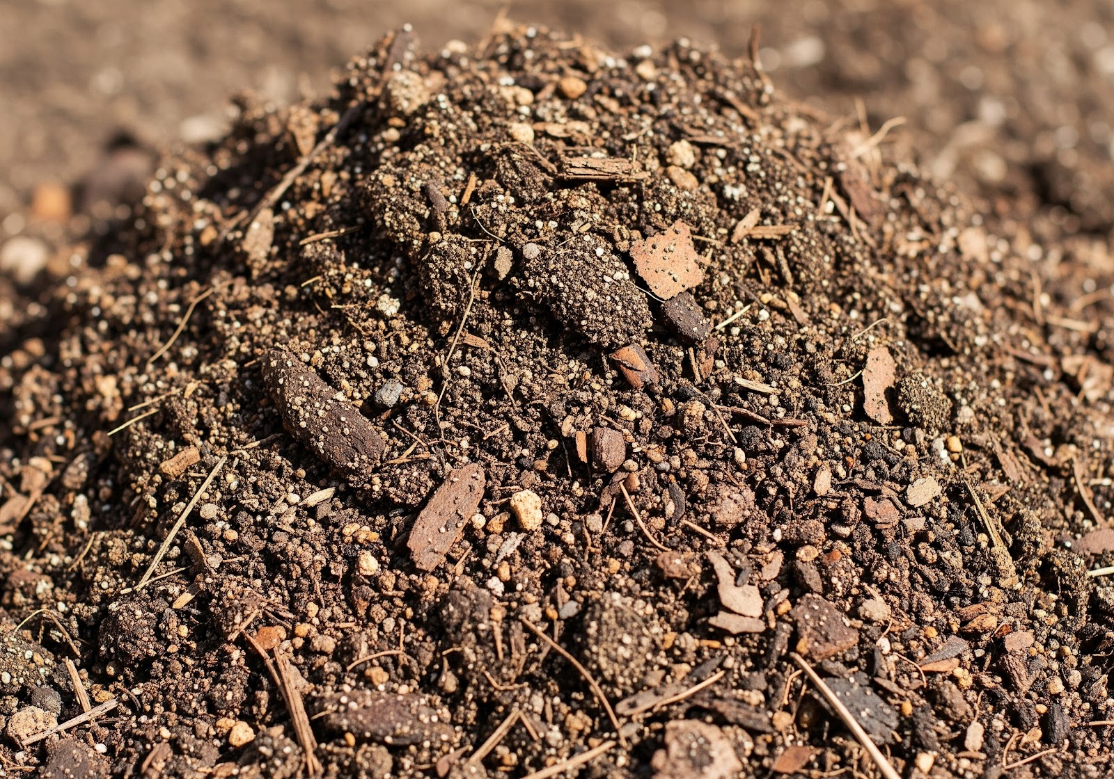 Uma pilha de solo misturado com terra vegetal escura, areia e alguns pedaços de composto orgânico, pronto para ser colocado em um vaso.