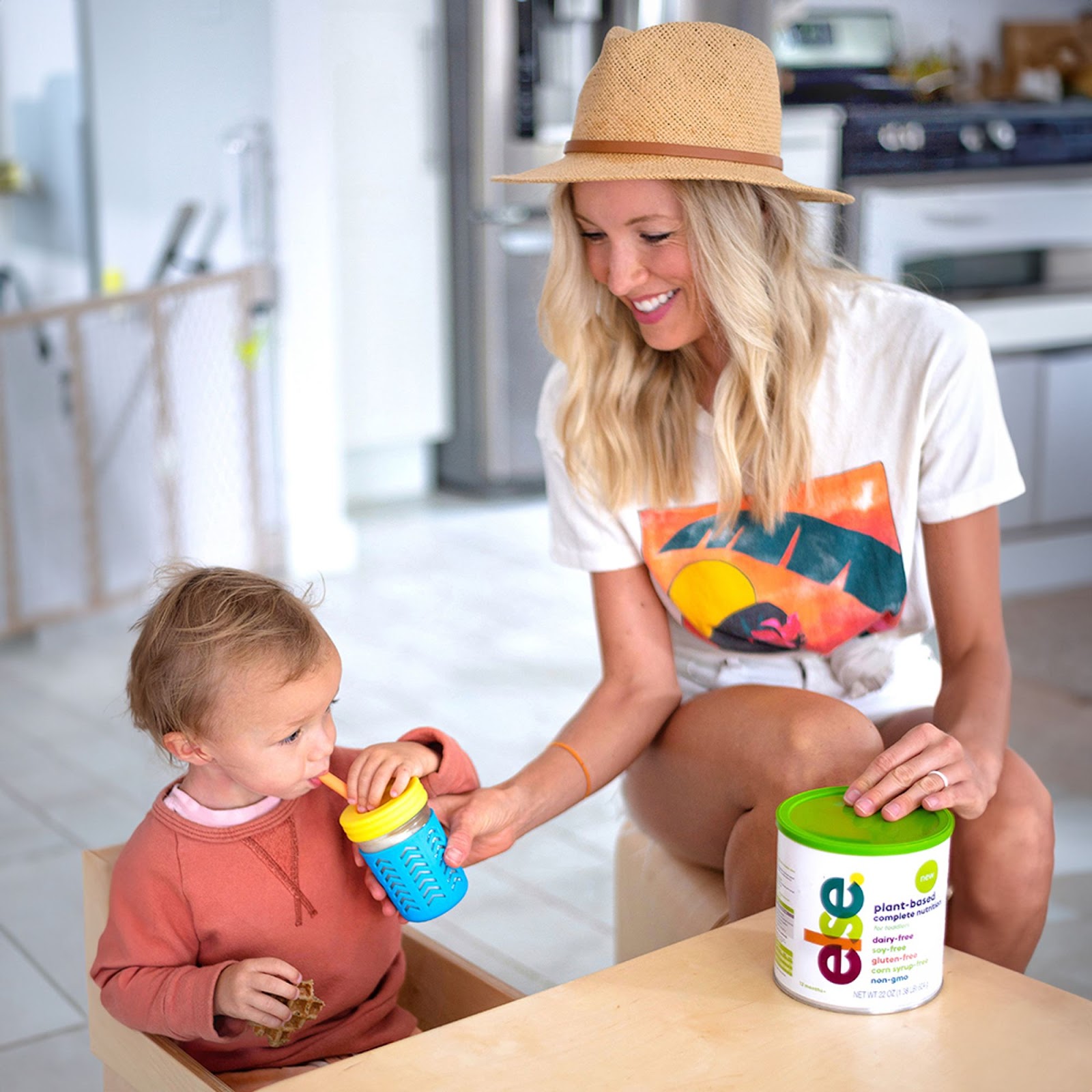 A toddler smiling while holding a plant-based formula bottle, showcasing a happy and healthy choice for nutrition.