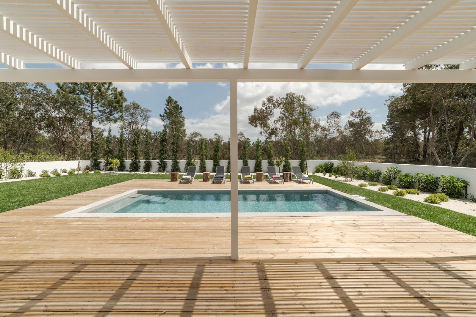 Patio cover in a backyard next to a pool, grass, and lawn chairs. 