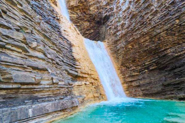 Cascada en los Pirineos aragoneses con paredes de roca estratificada y agua turquesa al pie

