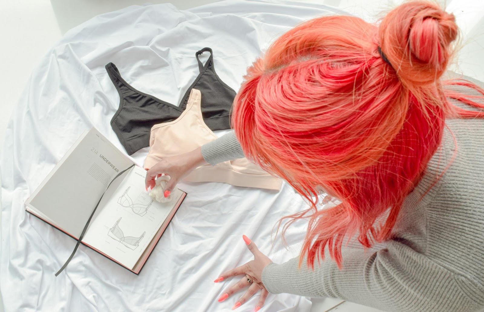 A young woman with pink hair designs fashion, showcasing bras and creativity.