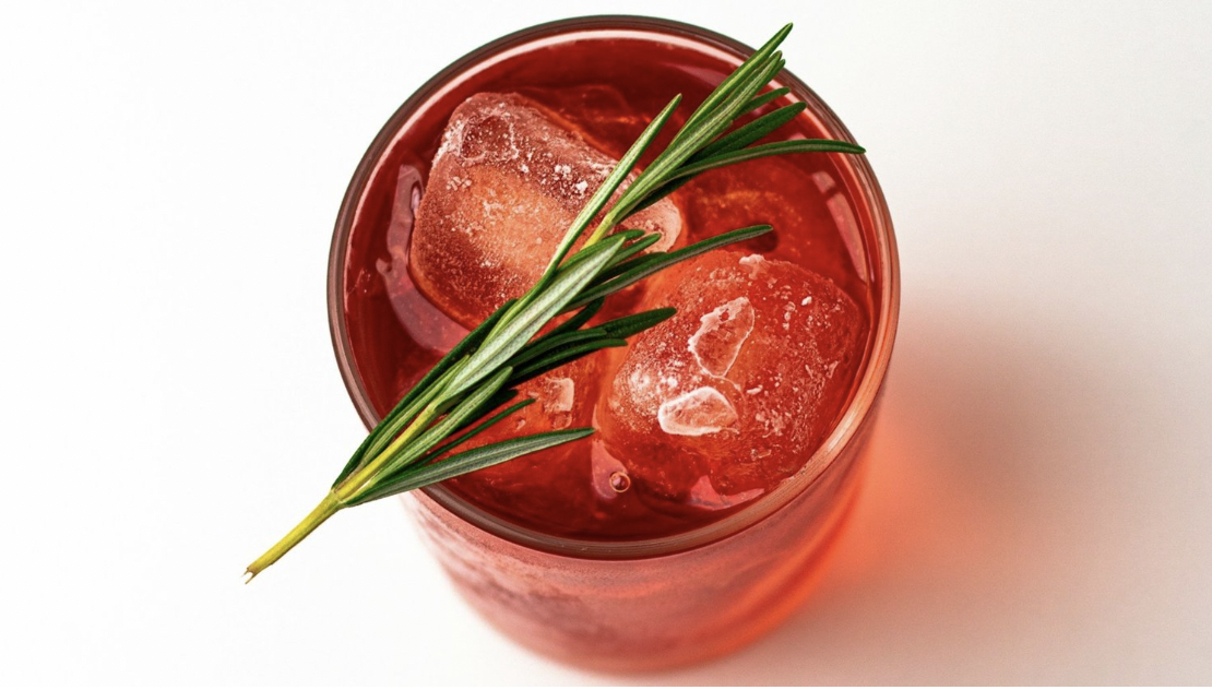 A rosemary sprig sits on top of a rocks glass filled with a Negroni cocktail