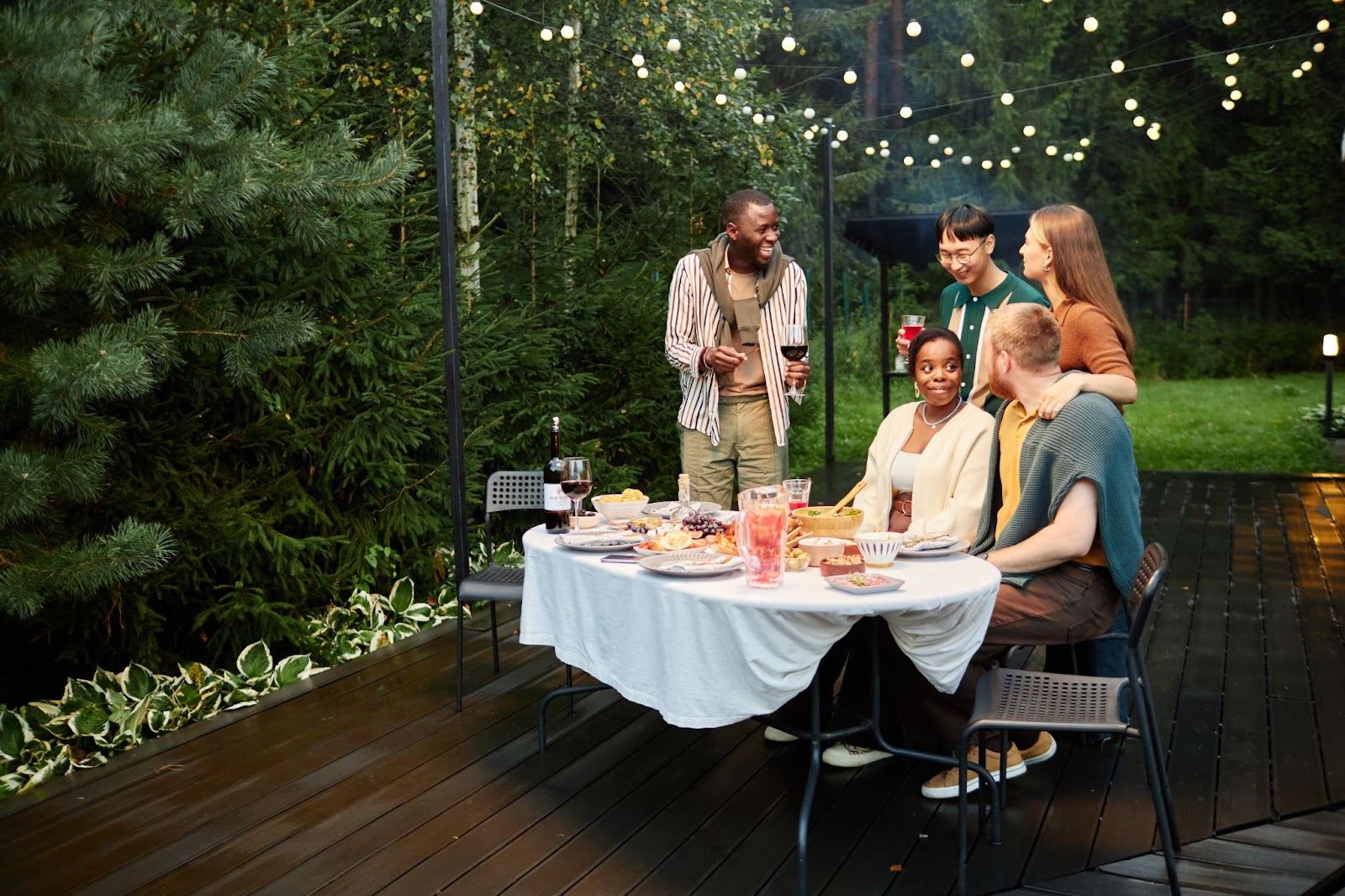 Friends drink wine on a deck illuminated by LED lights.  