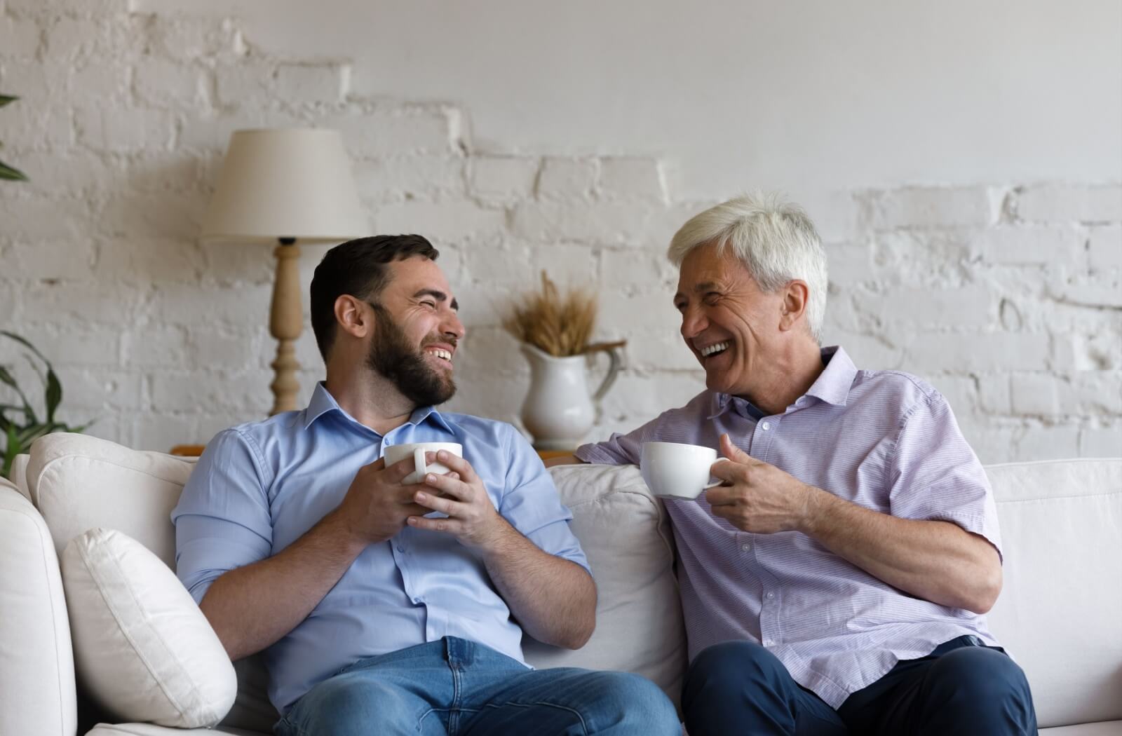 A senior and their adult child laugh as they connect and enjoy a tea together.
