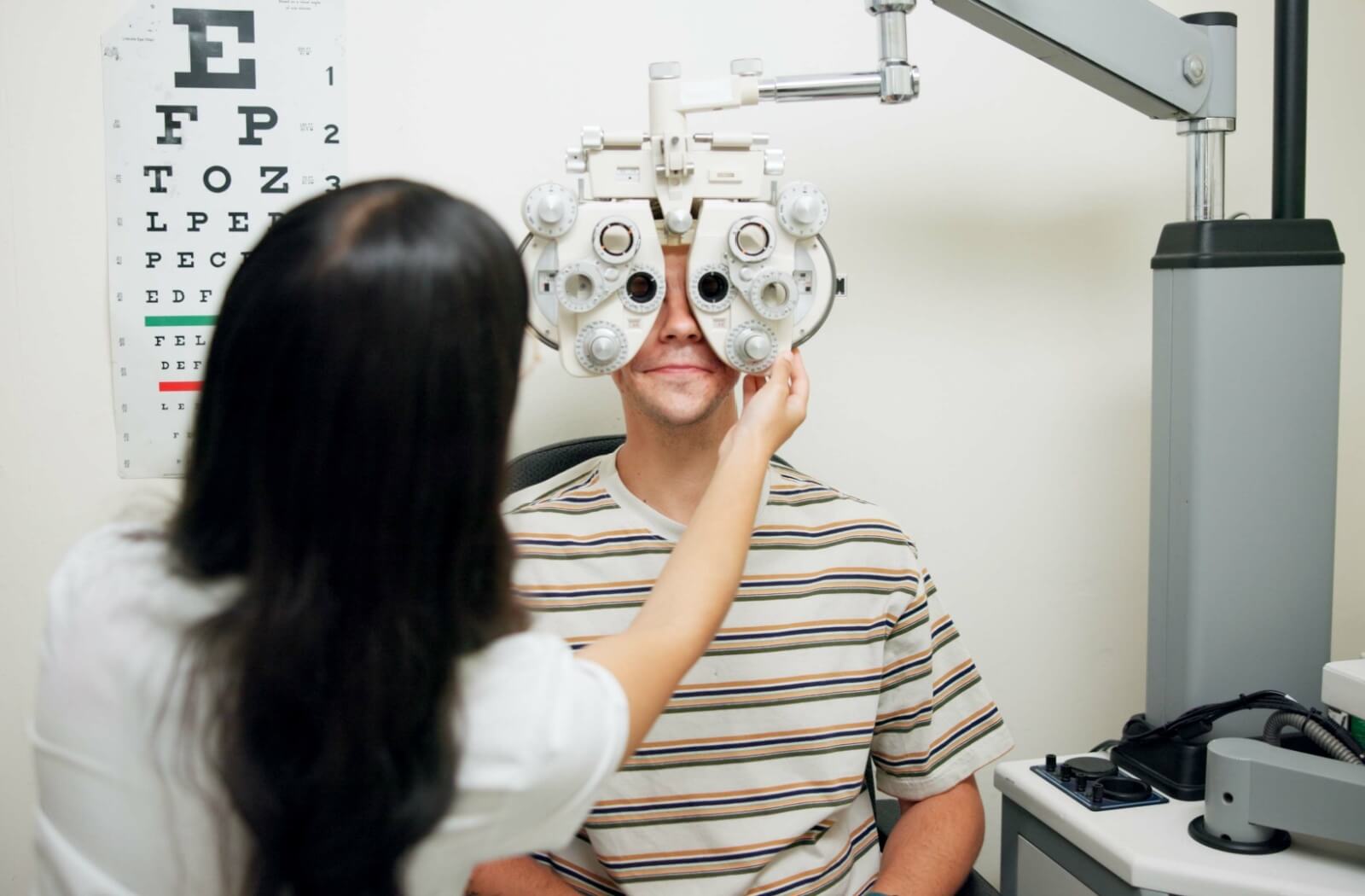 An optometrist using a phoropter to assess their patient's vision during their routine eye exam.