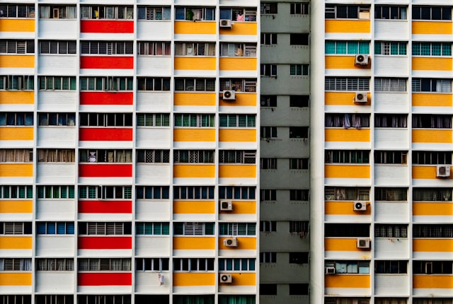 A colorful residential building facade, designed by architects with a focus on sustainability, features horizontal bands in red, orange, and white.