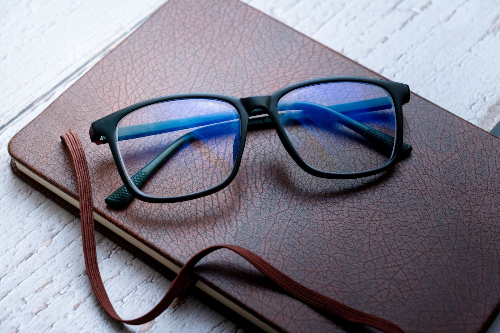 A pair of blue light glasses resting on a notebook.
