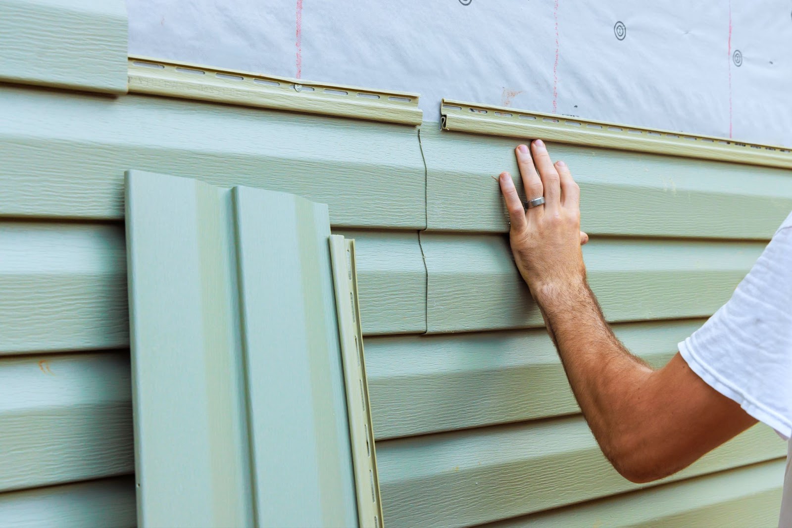 A close-up of a builder's hand installing sidings. 