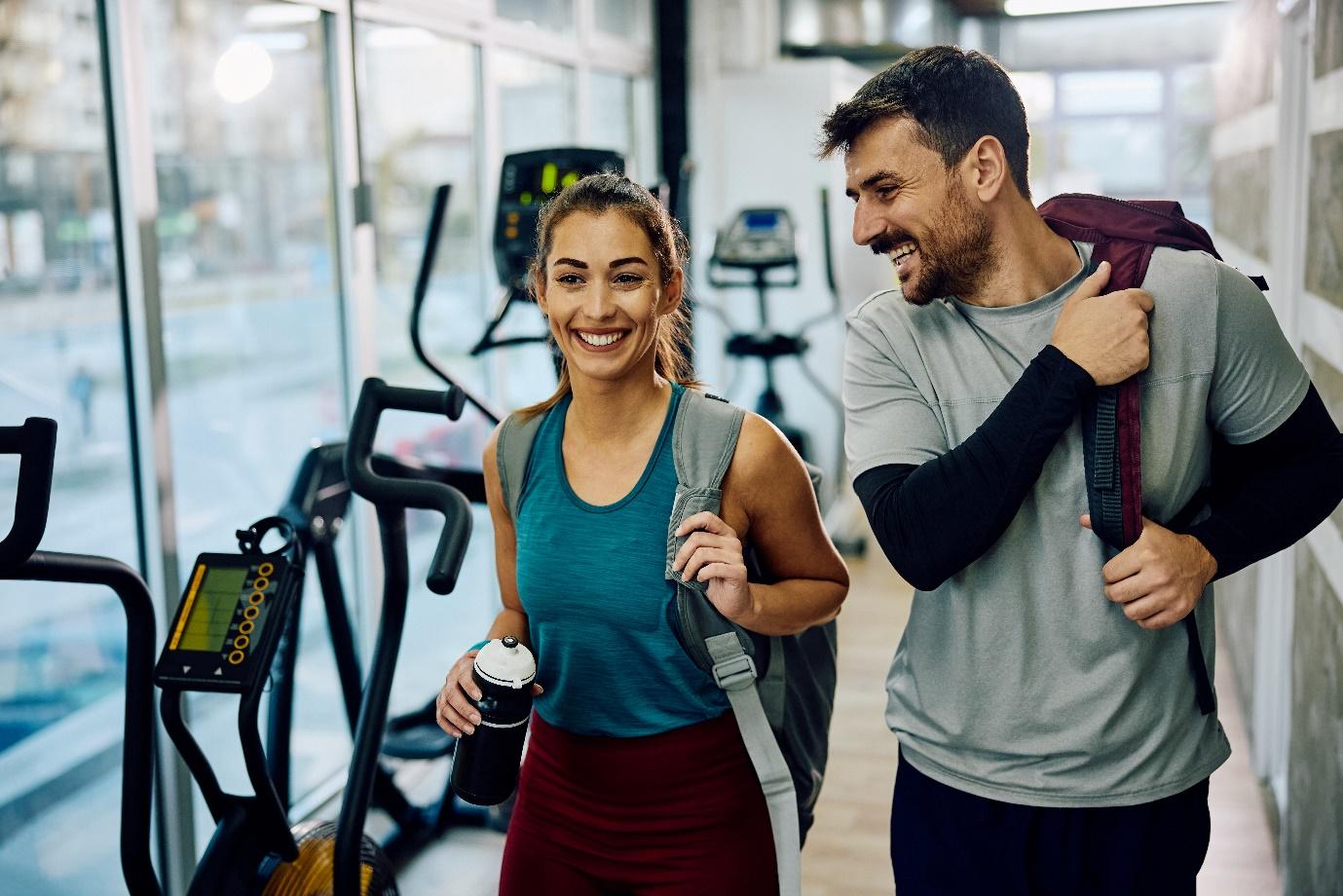 Pareja joven sonriente saliendo del gimnasio después de entrenar, promoviendo un estilo de vida saludable y activo