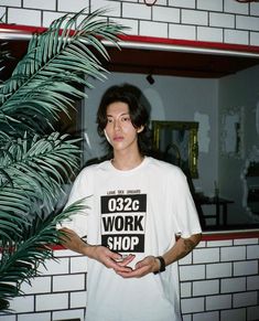 This contains an image of Kim Tae I  standing in front of a mirror with his hands on his hips while wearing a t - shirt that says work shop