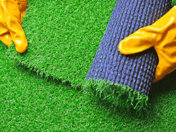 Worker handling artificial grass roll – is artificial grass safe for installation in homes and schools?