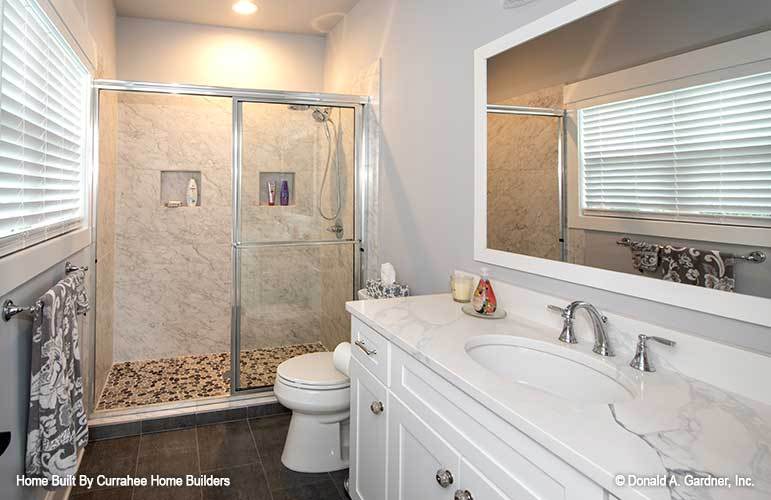 Bathroom with a marble top vanity, a toilet, and a walk-in shower enclosed in sliding glass doors.