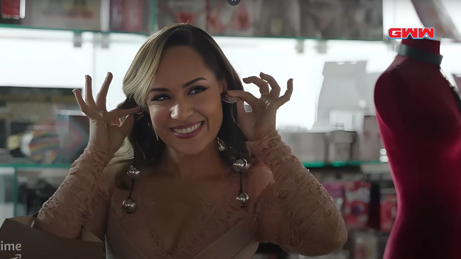 Grace Byers wearing earrings and a beige lace dress smiling brightly.