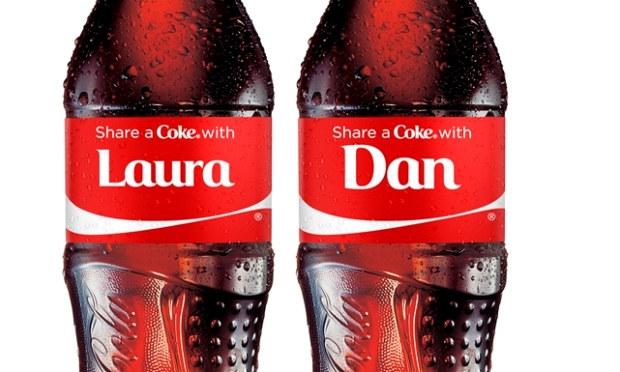 Dve fľaše Coca-Cola s personalizovanými etiketami „Share a Coke with Laura“ a „Share a Coke with Dan“. Fľaše sú pokryté kvapkami vody, čo naznačuje ich osviežujúci charakter, a majú typický červený dizajn Coca-Cola.