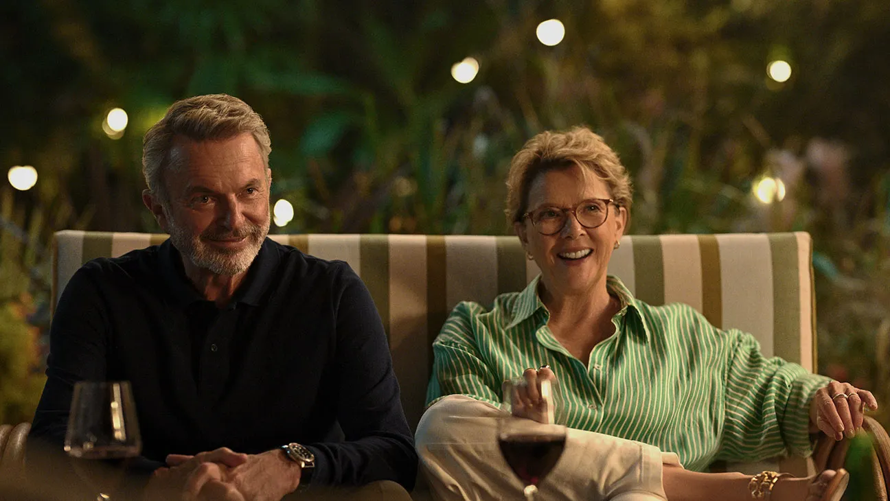 Dos personas sentadas en un sofá al aire libre, disfrutando de una conversación por la noche. A la izquierda, un hombre con barba y camisa oscura, y a la derecha, una mujer con gafas y camisa a rayas verde y blanca.