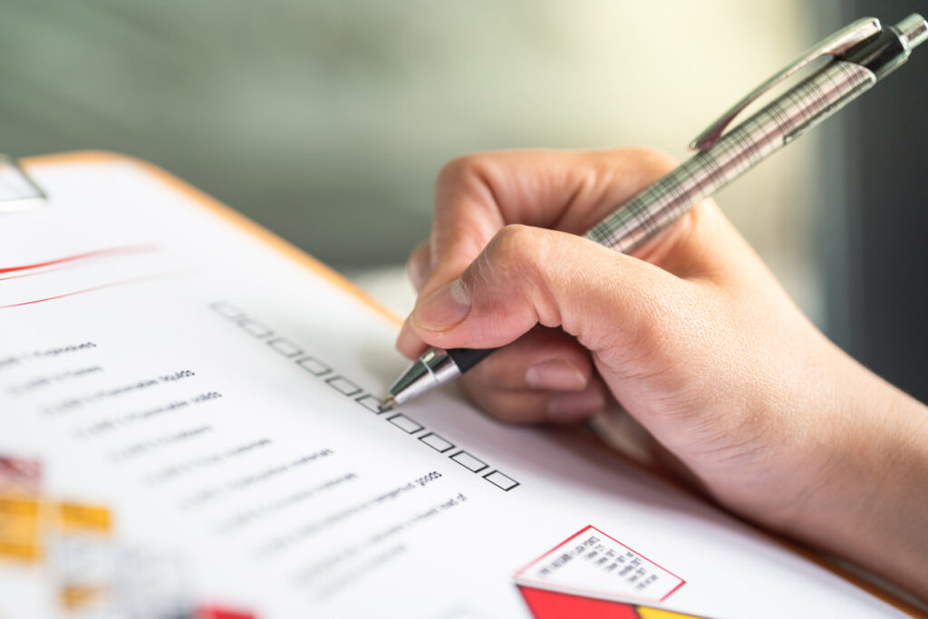 Hand filling out a quality control checklist form for product safety assurance