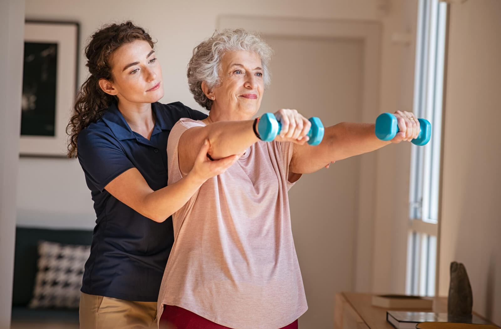 A caregiver helping an older adult in assisted living use small blue weights to build strength and keep their joints healthy.