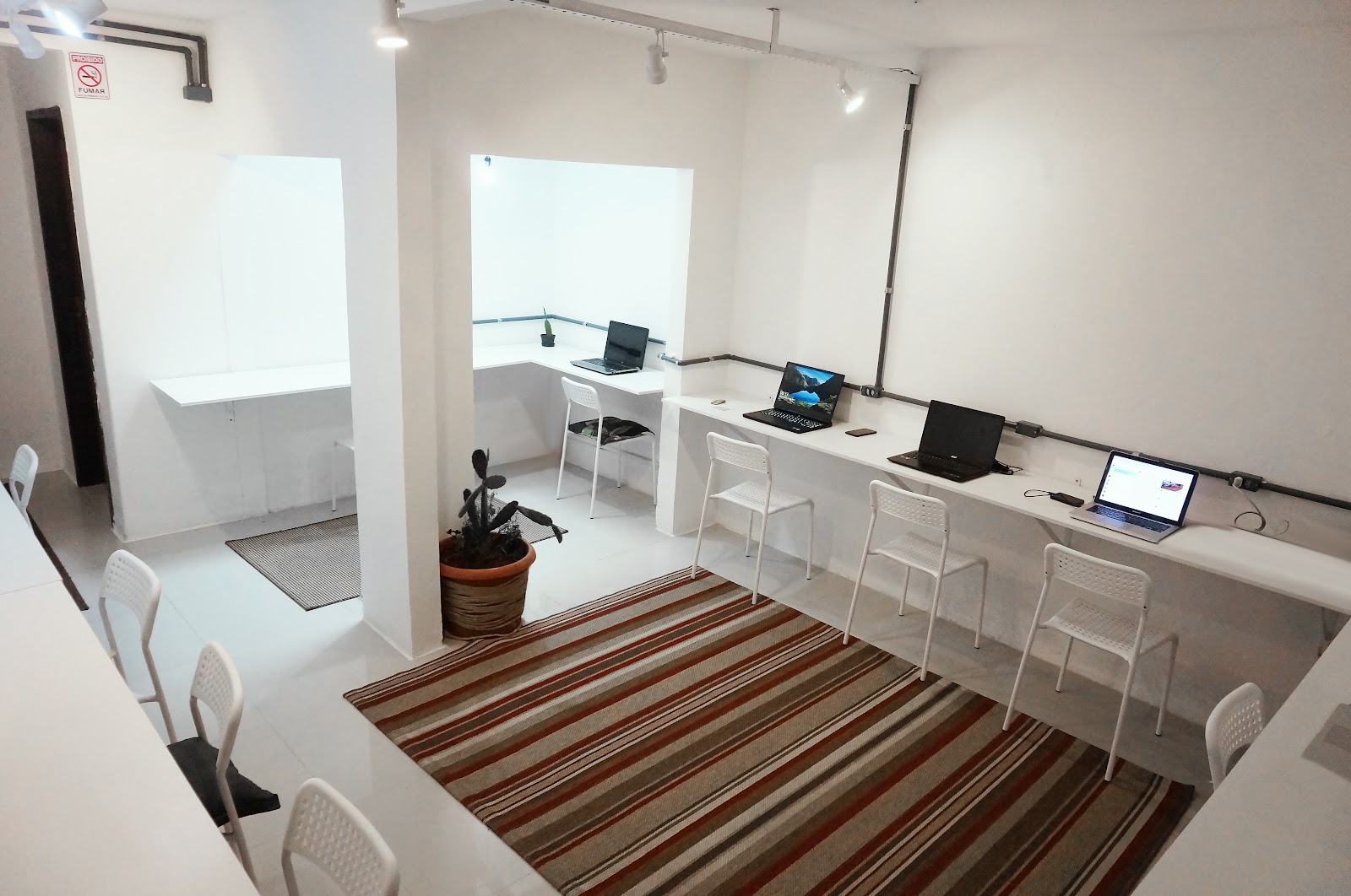Imagem vista do cowork, com cumputadores e cadeiras bem organizados ao longo de uma bancada. 