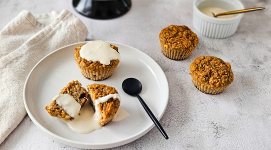 Une assiette avec des muffins aux carottes et aux lentilles garnis de crème, avec d'autres muffins exposés sur un présentoir à gâteaux en arrière-plan.