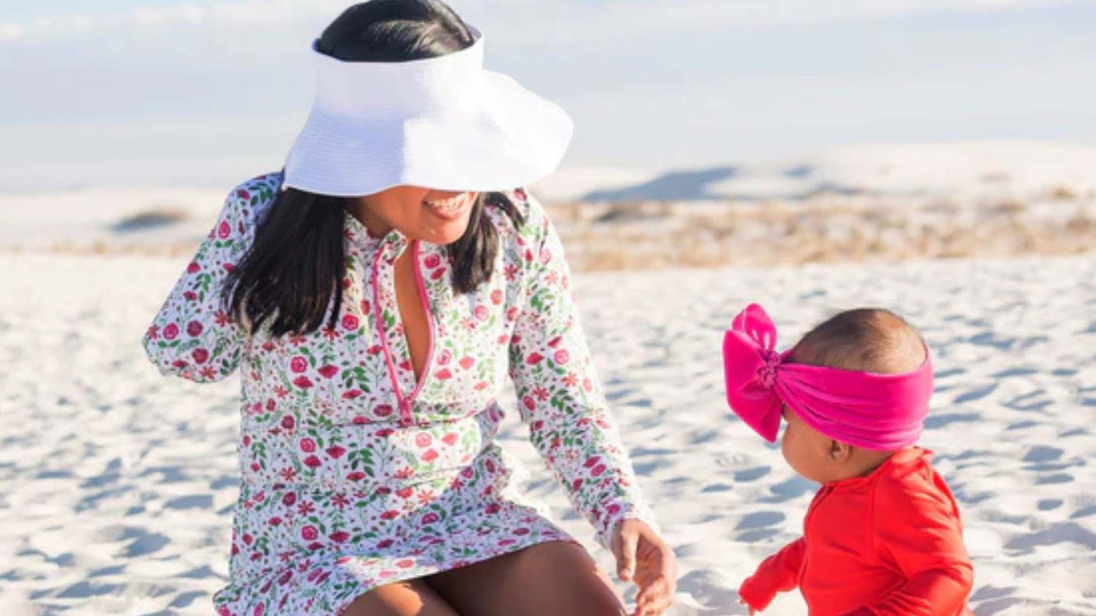 Woman with wide brim sun visor by SwimZip with her baby at the beach—Sunburn safety: All you need to know to stay safe in the sun