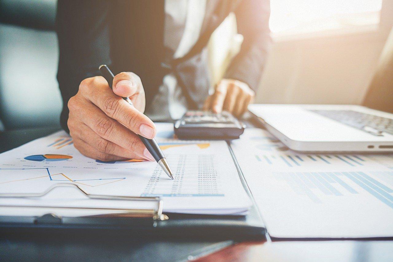 Um homem  em frente a uma mesa com a calculadora na mão analisando planilhas financeiras.