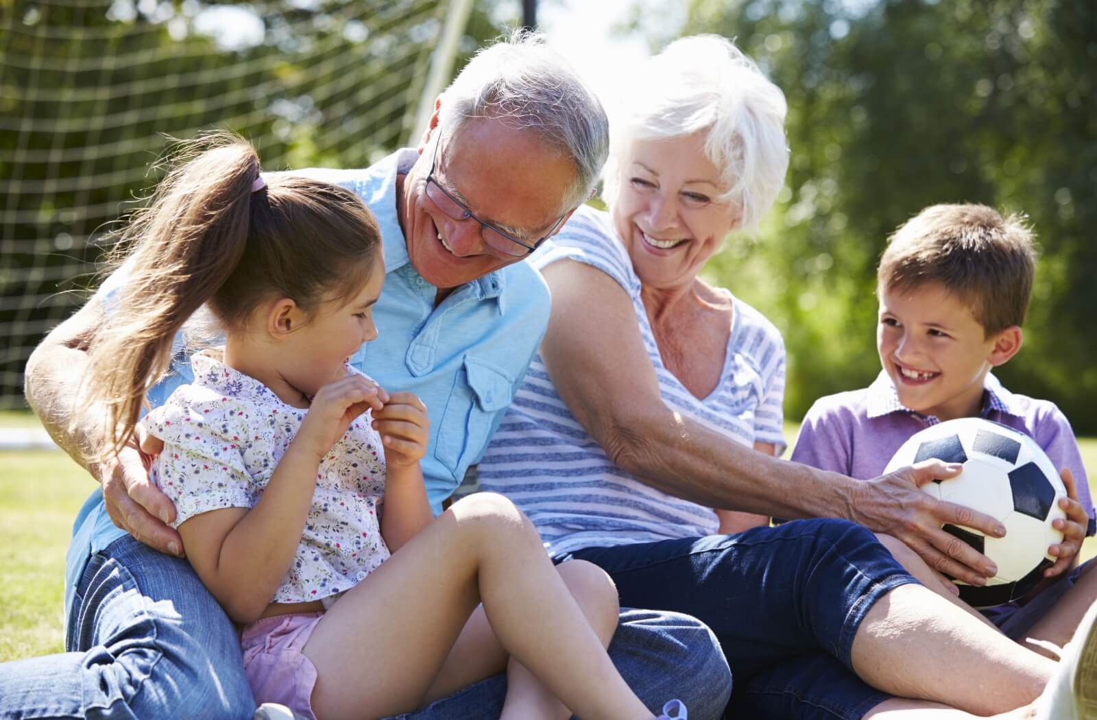 Energetic grandparents take a break from playing soccer & sit with their grandkids.