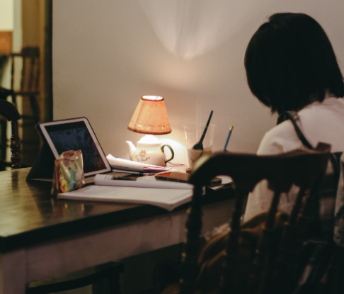 Writing essays for top grades. A lady sits at her dining room table with her laptop open in front of her and a textbook flat n the table. She tries to understand how to write an essay that will captivate her audience.