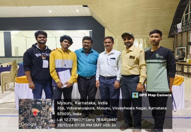 Group photo of students and faculty members at a tech event in Mysuru, Karnataka, captured with GPS map camera on December 26, 2024, showing participants smiling and posing indoors after the event.