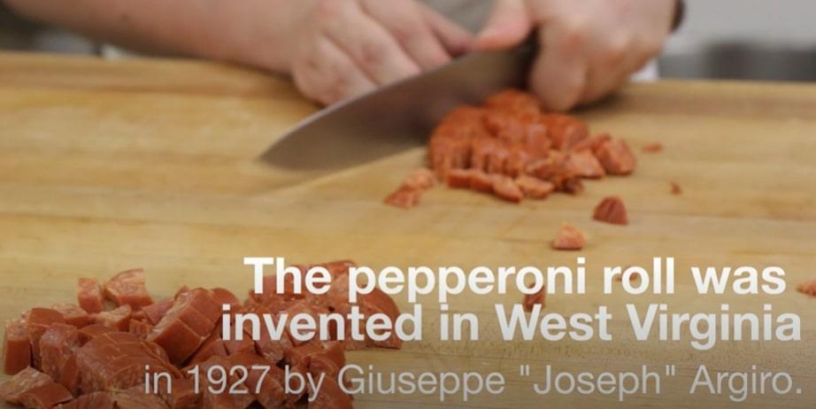 Screengrab from Nu-Era bakery's video, showing pepperoni being chopped. The text overlay reads "The pepperoni roll was invented in West Virginia in 1927 by Giuseppe 'Joseph' Argiro."