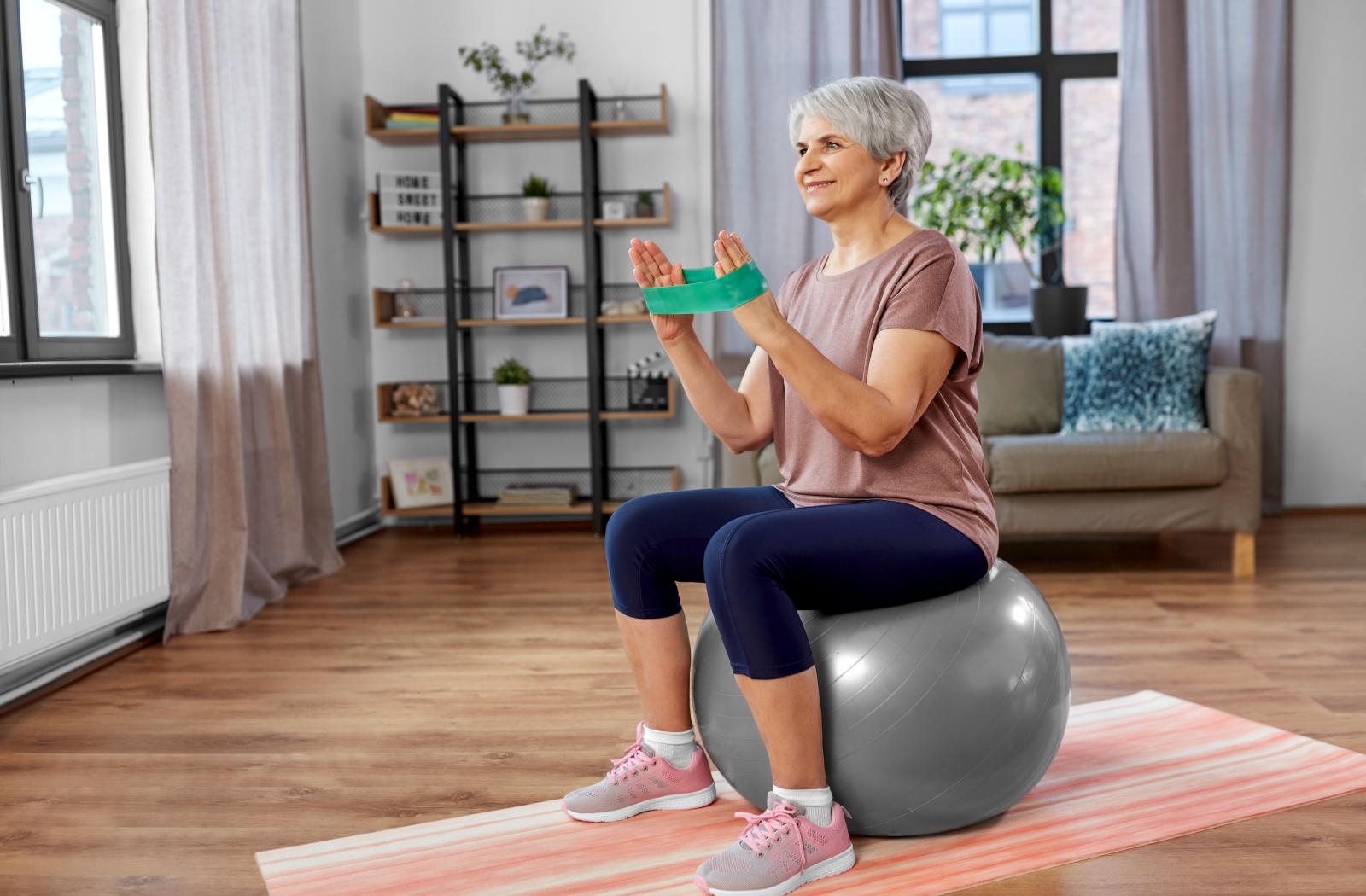 A senior sits on an exercise ball with a band, practicing balance.