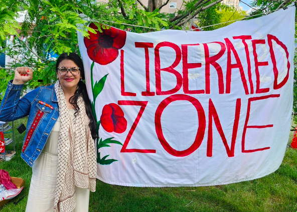 Photo of Representative Tlaib standing in front of a sign that reads "liberated zone"