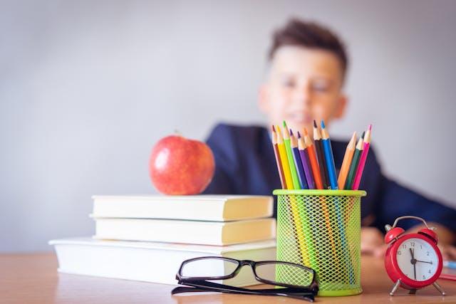 A boy looking at books and pencils on the desk in front of him