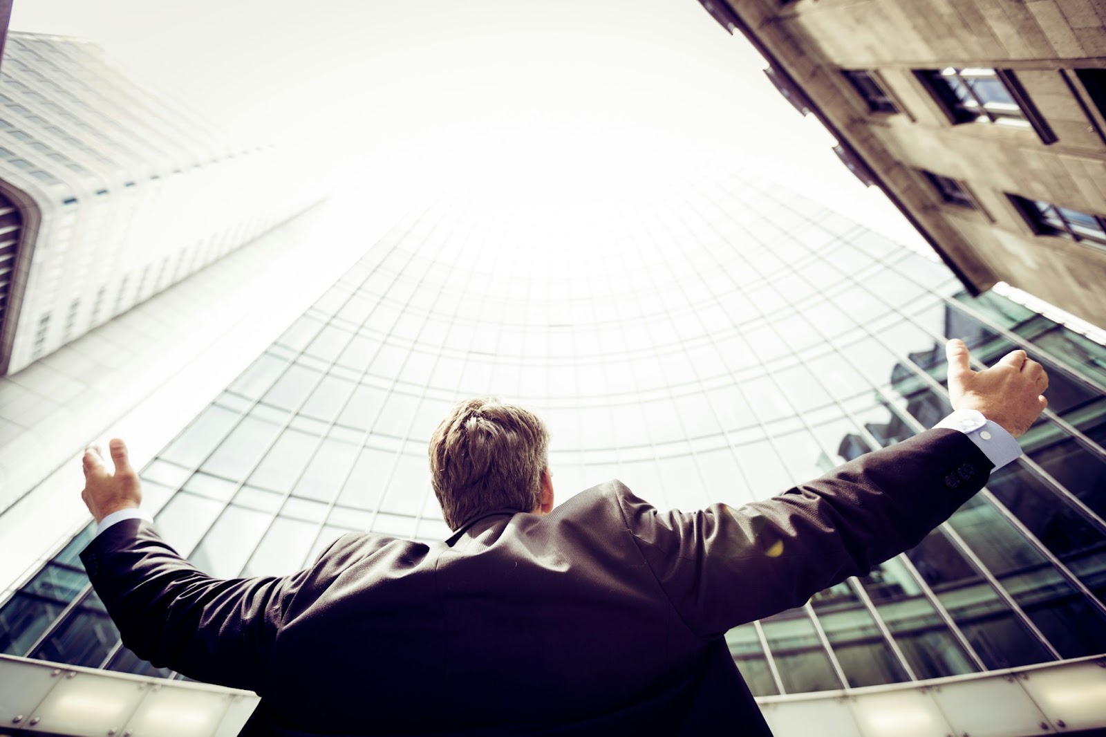 Man with his arms open towards the sky in the middle of tall buildings