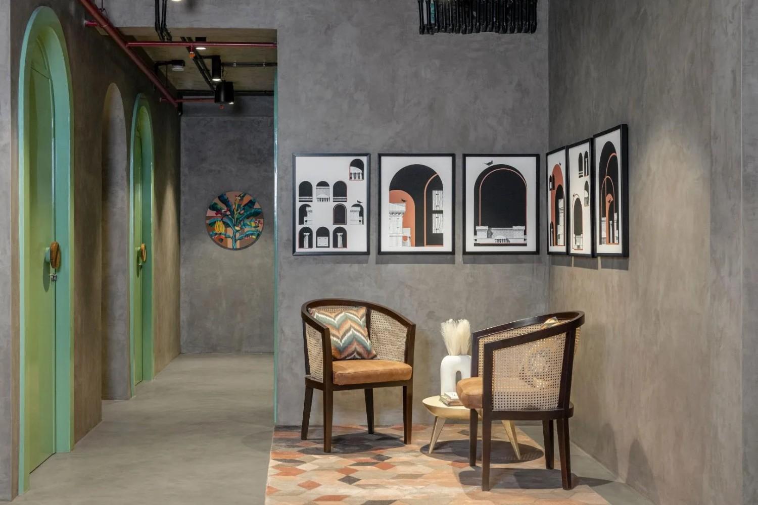 A modern workspace interior features two wooden chairs with woven backs and patterned cushions facing a small white table with a vase on top.