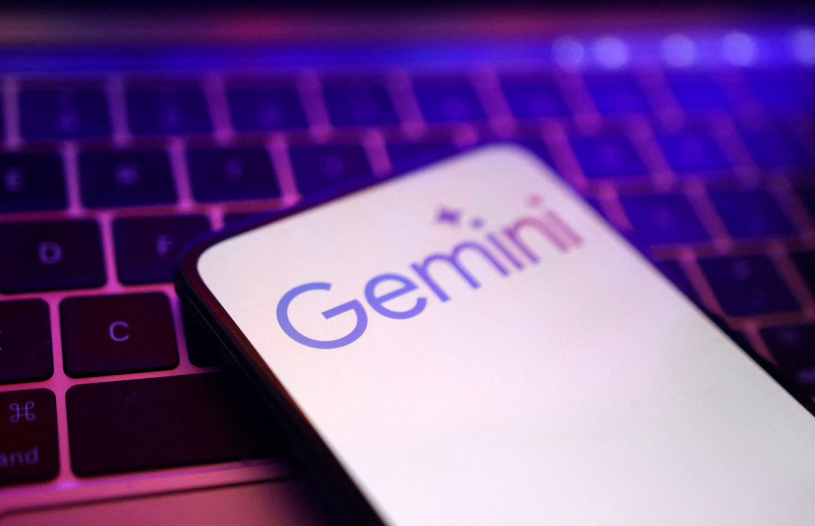 Pantalla de un smartphone mostrando el logo de Gemini sobre un teclado iluminado con luz violeta.