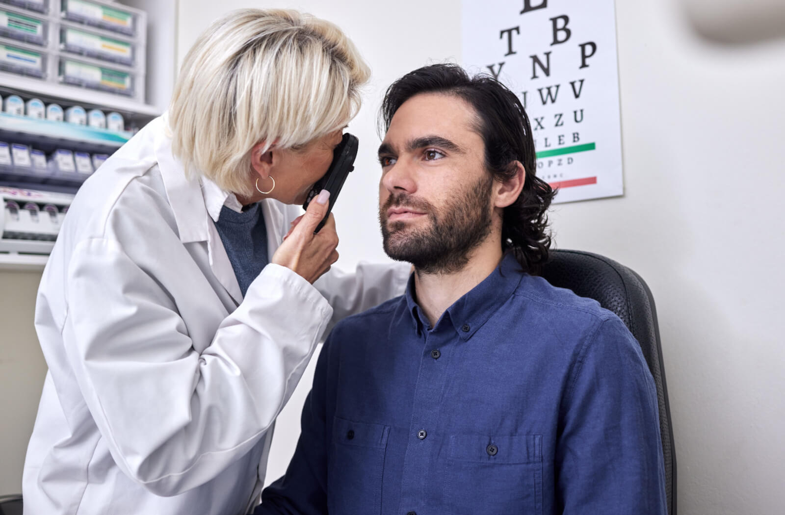 An optometrist carefully examining a patient's eyes during an eye exam to determine if he needs prescription medication.