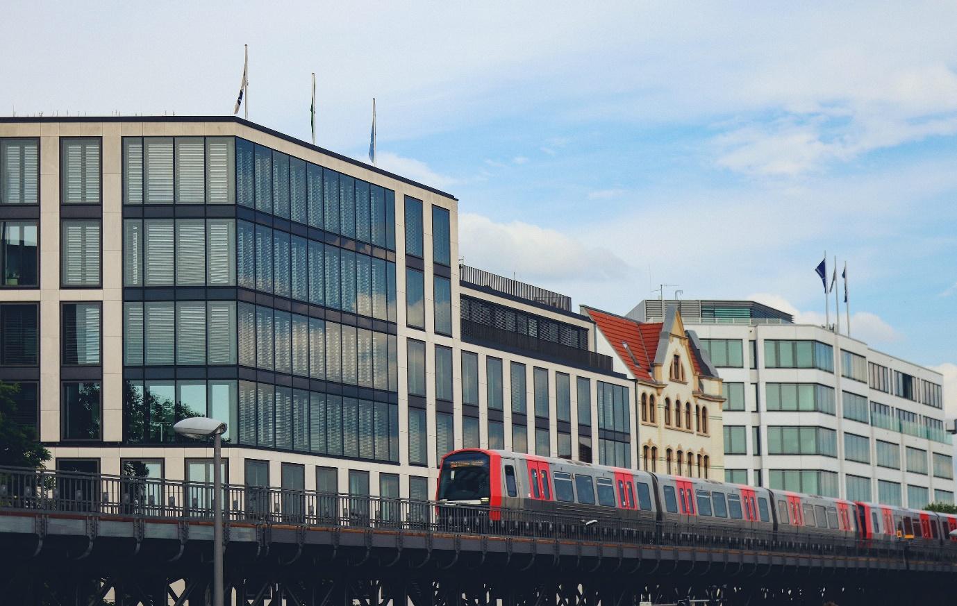 A red train traveling over a bridge next to tall buildings