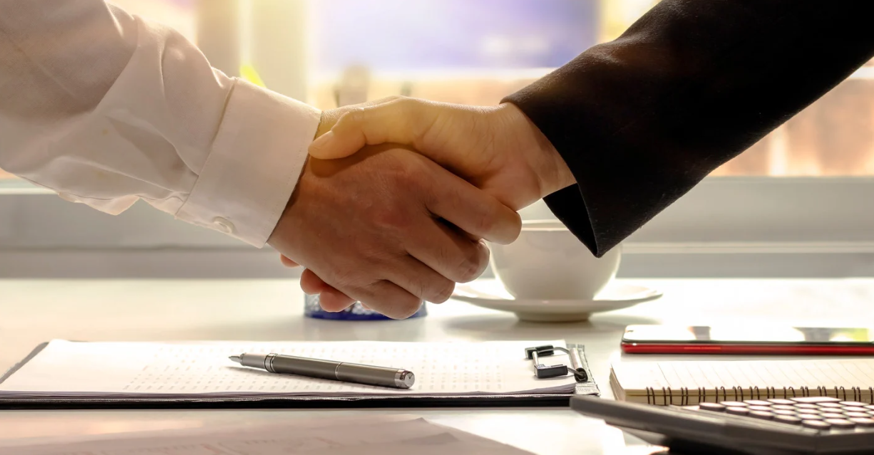 (Two people shake hands over a desk with paperwork, symbolizing a successful debt settlement or financial agreement.)