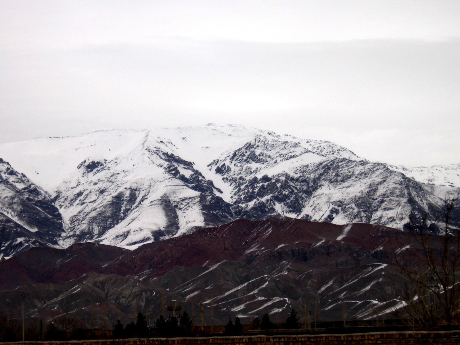 Snow-capped Binalud Mountain in Iran, showcasing rugged peaks and slopes covered in snow, with a mix of brown and green foothills, offering a stunning winter landscape.